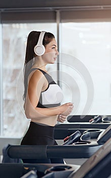 Sportive girl in headset enjoying music while running on treadmill at health club