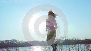 Sportive girl jogging along the river bank during sunrise or sunset. Healthy lifestyle concept of athletic woman goes in