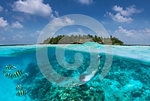 Sportive girl snorkels in turquoise waters over a coral reef in the Maldives