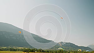 Sportive group of people fly on paragliders with blue sky and mountains on background. Paraplane runway. Flying on paraglider in A