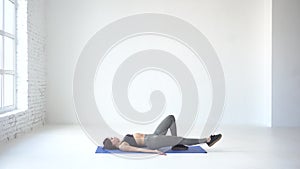 Sportive healthy woman is lying on the exercise mat and lifting up her leg to warm up. 4k footage.