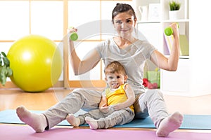 Sportive laughing mother with baby and dumbbells in hands. Motherhood is not a cause to let oneself go