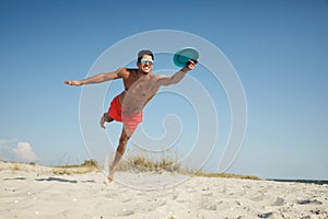 Sportive man jumping and catching flying disk at beach