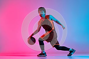 Sportive man playing basketball  on gradient pink blue studio background in neon light. Youth, hobby, motion