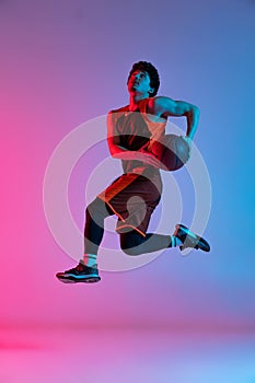 Sportive man playing basketball isolated on gradient pink blue studio background in neon light. Youth, hobby, motion