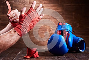 Sportive man wrapping his hands with bandage and boxing gloves on wooden plank.