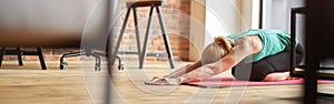 Sportive mature blonde woman practicing yoga, sitting in Child pose on the floor at home in modern apartment