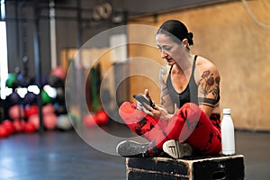 Sportive mature woman using phone on a cross training gym