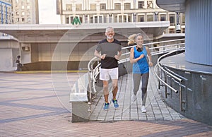 Sportive middle aged couple, man and woman in sportswear looking happy while running together outdoors, having cardio