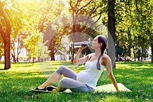 Sportive pregnant woman drinking water in park