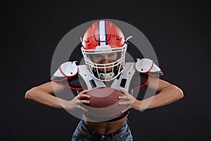 Sportive serious woman in helmet of rugby player holding ball and screaming aggressively.