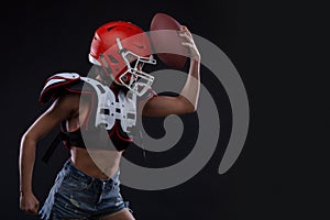 Sportive serious woman in helmet of rugby player holding ball in stuio on dark background.