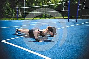 Sportive woman doing push-ups on the blue tennis court in Moscow Yauza park