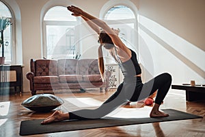 Sportive woman doing yoga in Virabhadrasana pose at home