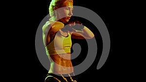 Sportive woman, female professional boxer training in dark smoky gym in neon light. Sport, action, power, energy concept