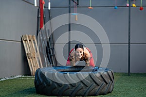 Sportive woman flipping a huge wheel in the gym