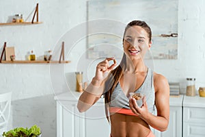 Sportive woman holding almond and smiling at home