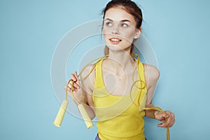 Sportive woman holding a skipping rope yellow tank top exercise gymnastics blue background