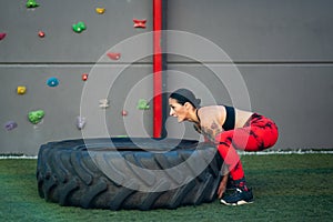 Sportive woman lifting a truck wheel in a gym