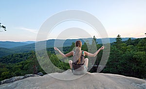 Sportive woman meditating alone taking a break on hillside trail. Female hiker enjoying view of evening nature from