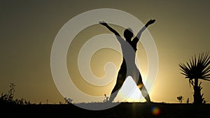 Sportive woman performing yoga pose, standing with raised hands against sunrise