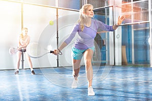 Sportive woman playing padel together with a partner. View through tennis net