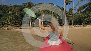 Sportive woman rows pink plastic canoe along sea water