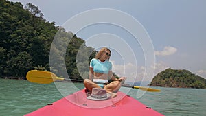 Sportive woman rows pink plastic canoe along sea water. Positive sports girl hand padding on kayak, front view.