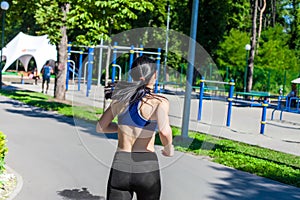 Sportive woman running along the path near sport playground