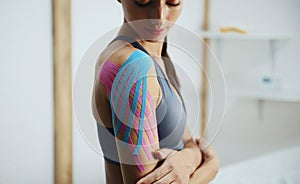 Sportive woman sits indoors with kinesio tape on her shoulder