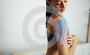 Sportive woman sits indoors with kinesio tape on her shoulder