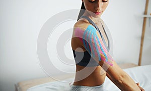 Sportive woman sits indoors with kinesio tape on her shoulder