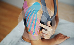 Sportive woman sits indoors with kinesio tape on her shoulder