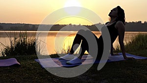 A Sportive Woman Sits And Raises Her Stomach on a Mat at a Lake Bank