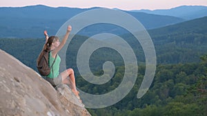 Sportive woman sitting alone taking a break on hillside trail. Female hiker enjoying view of evening nature from rocky