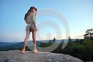 Sportive woman standing alone on hillside trail. Female hiker enjoying view of evening nature from rocky cliff on