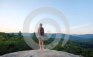 Sportive woman standing alone on hillside trail. Female hiker enjoying view of evening nature from rocky cliff on