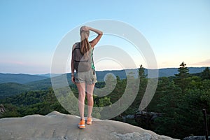 Sportive woman standing alone on hillside trail. Female hiker enjoying view of evening nature from rocky cliff on