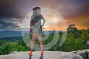 Sportive woman standing alone on hillside trail. Female hiker enjoying view of evening nature from rocky cliff on