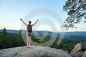 Sportive woman standing alone on hillside trail with raised up arms. Female hiker enjoying view of evening nature from