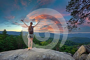 Sportive woman standing alone on hillside trail with raised up arms. Female hiker enjoying view of evening nature from