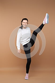 Sportive woman stretching one leg up in studio