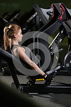 Sportive woman using weights press machine for legs. Gym.