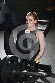 Sportive woman using weights press machine for legs. Gym.