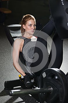 Sportive woman using weights press machine for legs. Gym.