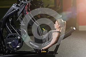 Sportive woman using weights press machine for legs. Gym.