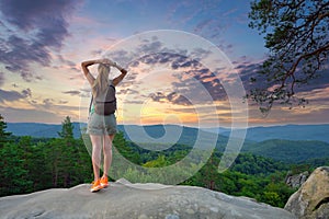 Sportive woman walking alone on hillside trail. Female hiker enjoying view of evening nature from rocky cliff on