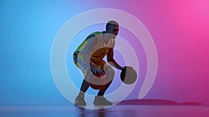 Sportive young male basketball player dribbling two basketball balls at once over gradient blue pink neon background