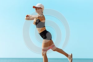 Sportive young woman, in sports black clothes, is engaged in fitness with elastic bands on the seashore, sports concept