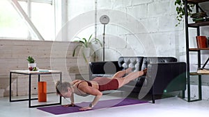 Sportive young woman with sporty athletic body doing push ups exercising on floor with legs on couch. Concept of healthy